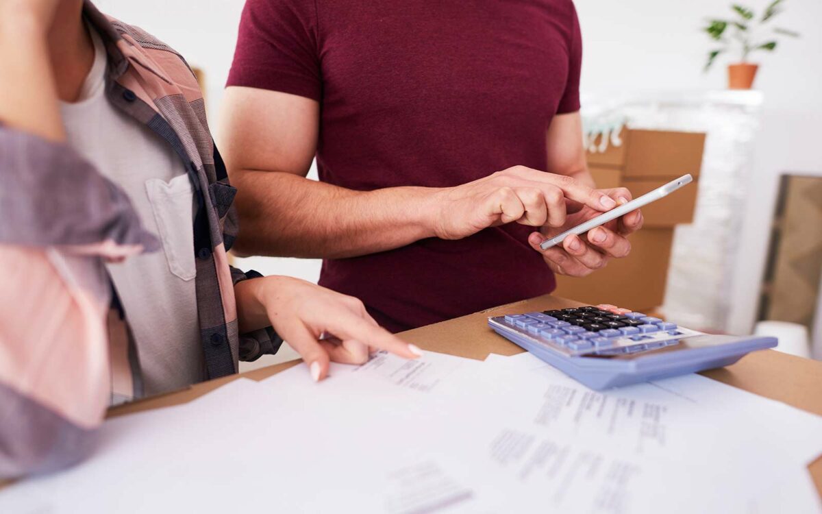 A view of a couple reviewing bills and using a calculator and smartphone to manage expenses
