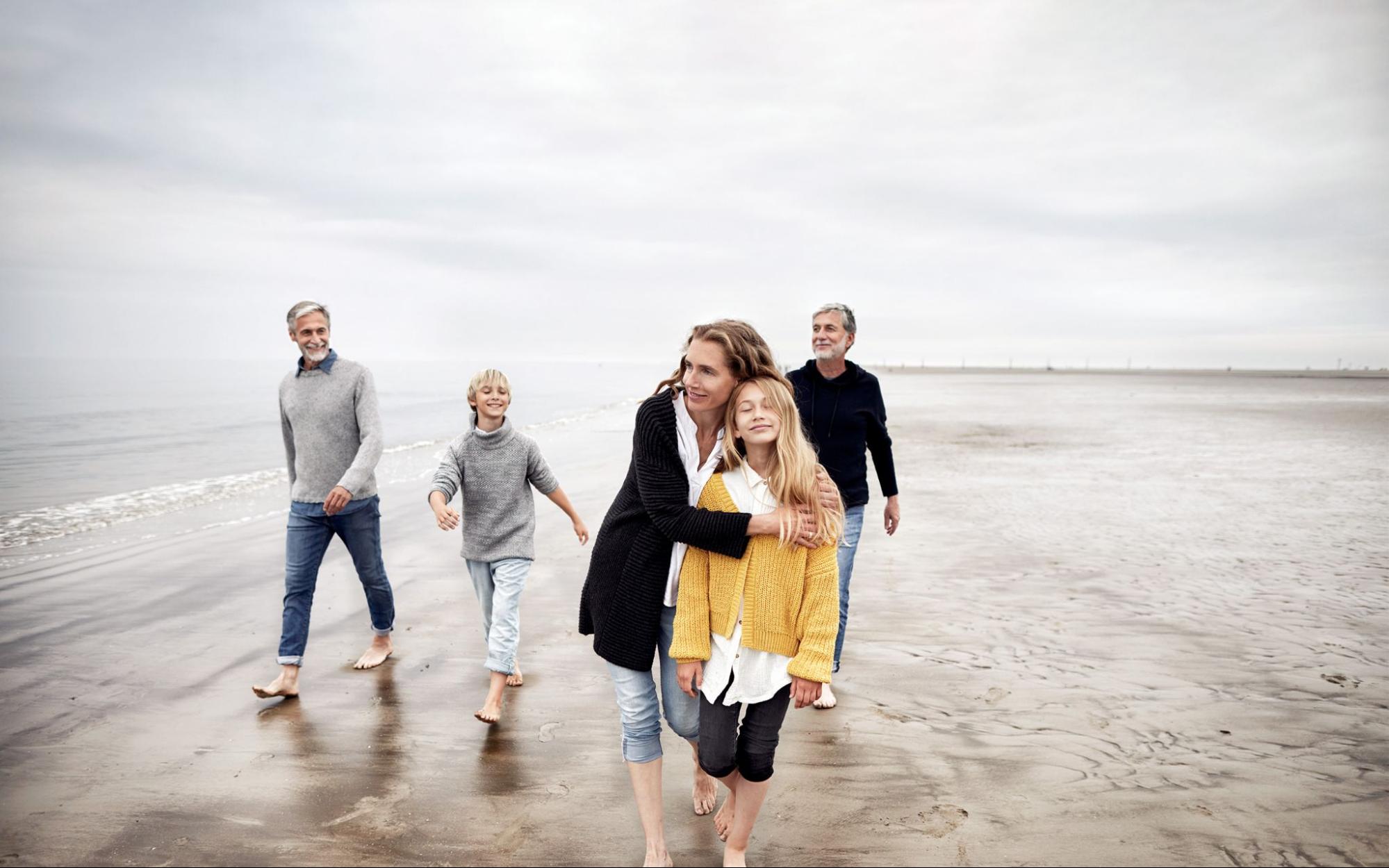 A view of multi-generational family walking barefoot on a beach, enjoying quality time together