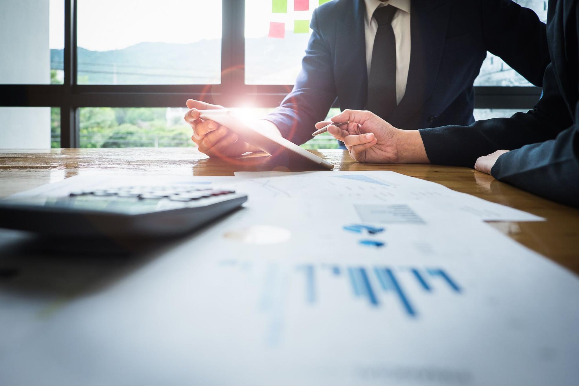 Business professionals reviewing financial charts and data on a tablet during a meeting at a modern office.
