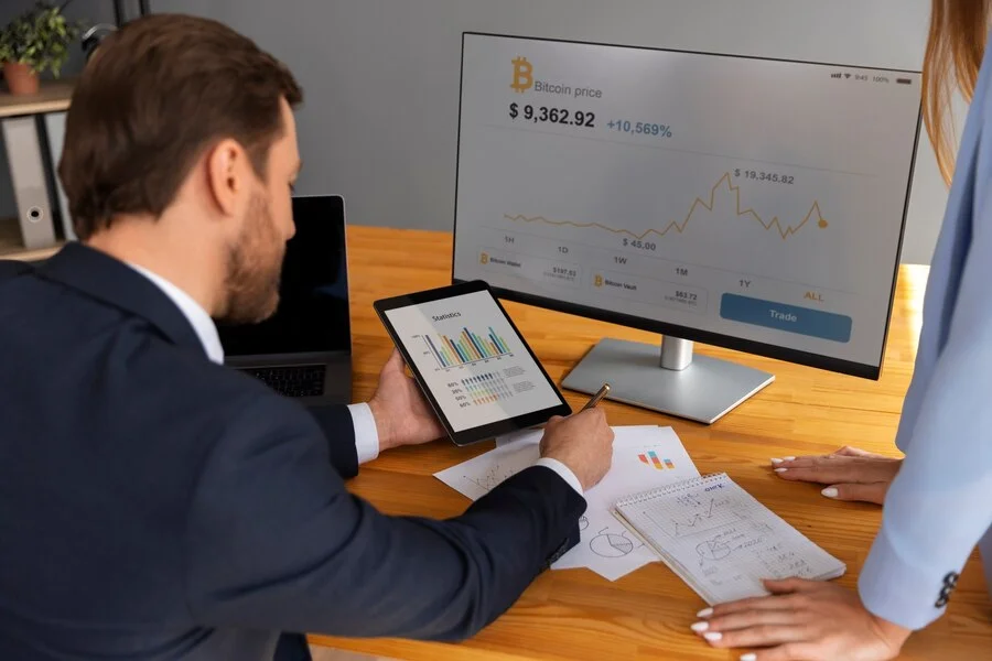 Businessman analyzing cryptocurrency charts on a tablet and monitor, with financial documents spread on the desk