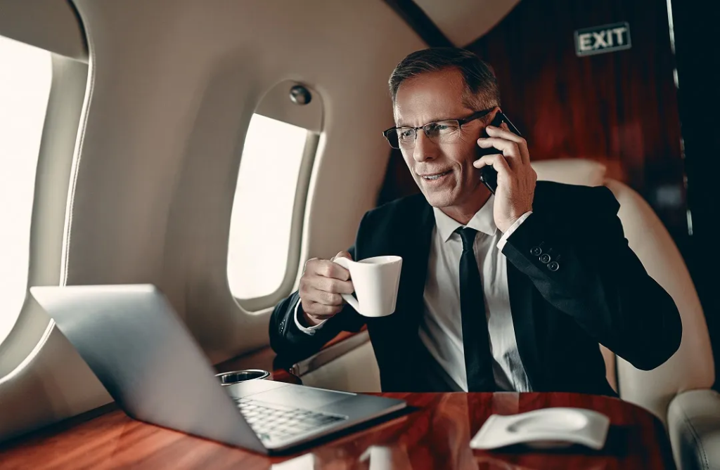 Businessman in a private jet holding a coffee cup, talking on the phone, and working on a laptop