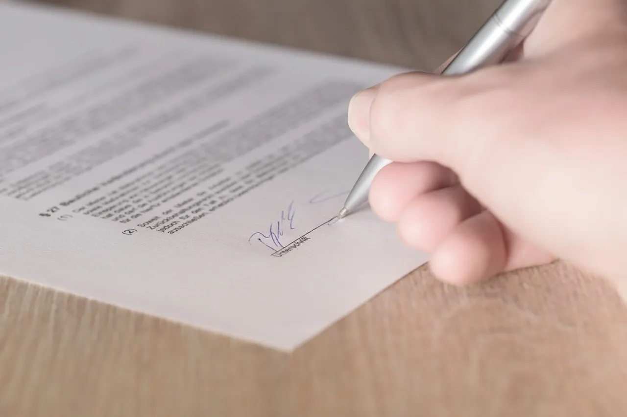 Close-up of a hand signing a legal document with a pen on a wooden table