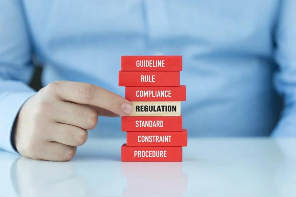 Hand pointing at stacked blocks labeled with compliance terms, highlighting Regulation at the center