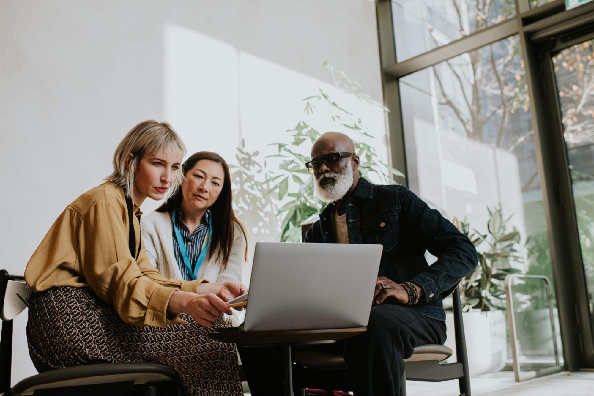 Three professionals sitting together and discussing something on a laptop in a bright, modern office space