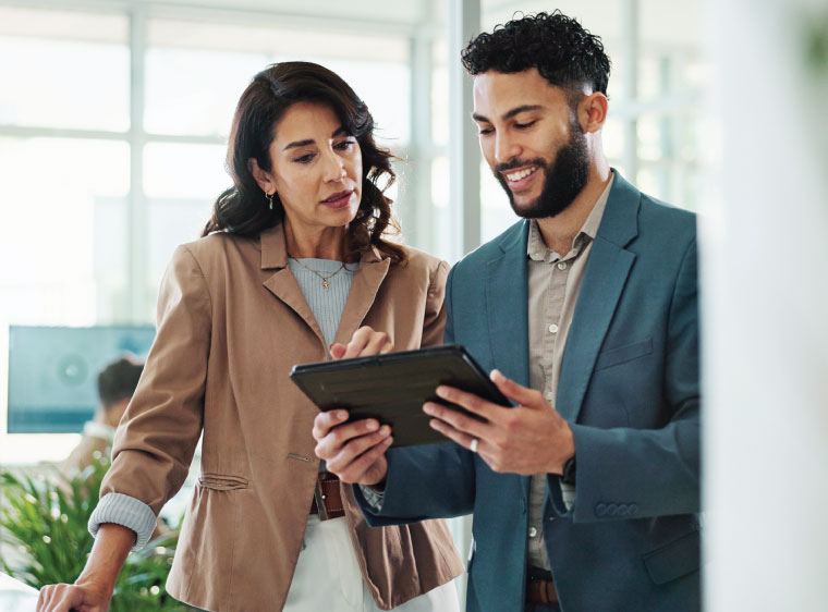 Two business professionals discussing data on a tablet in a modern office setting.