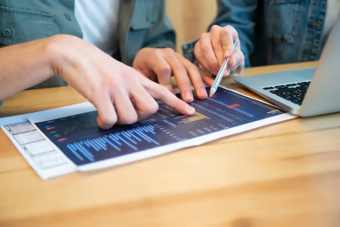 Two people reviewing a financial report with charts and graphs next to a laptop