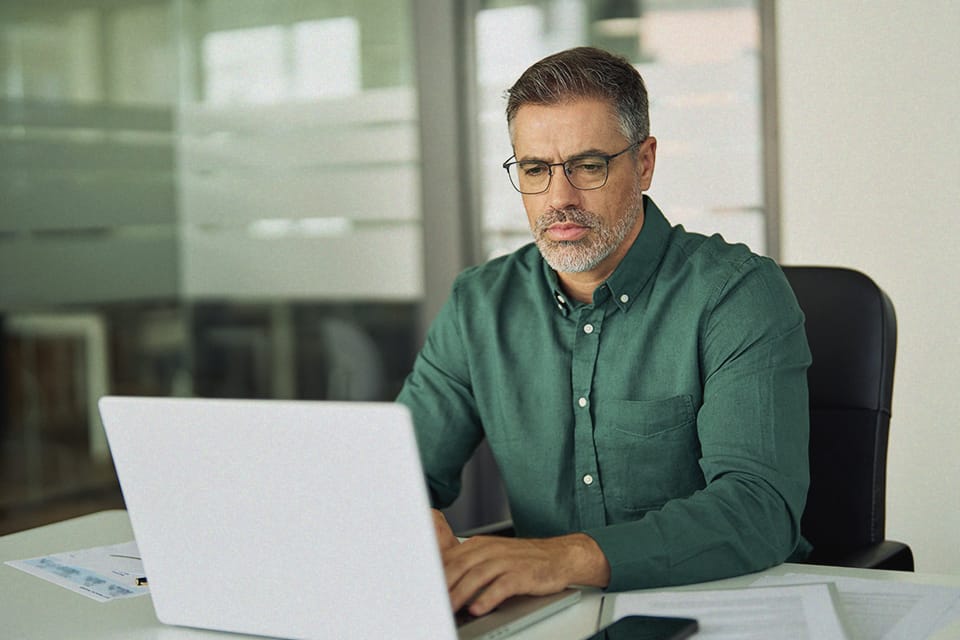 Focused man in glasses working on a laptop in an office, possibly reviewing third-party risk or business data
