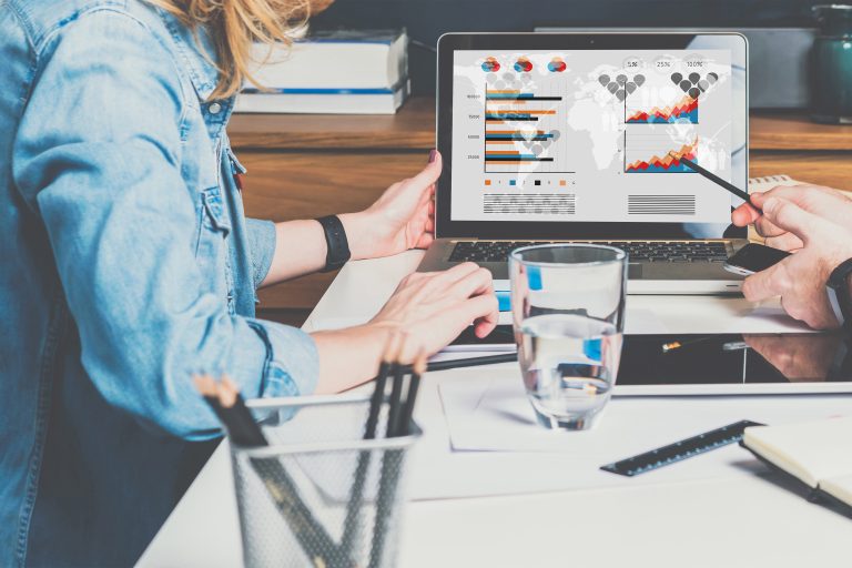 Businessman and businesswoman sitting at table in front of laptop and working. Graphs,charts and diagrams on PC screen